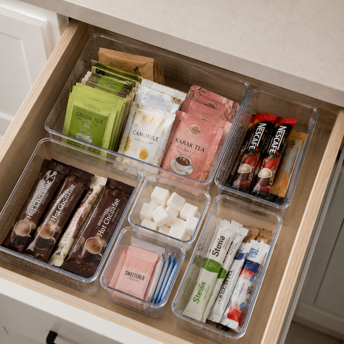Clear acrylic drawer organizers used in a kitchen drawer to neatly separate tea, coffee, sweeteners and snack sachets.