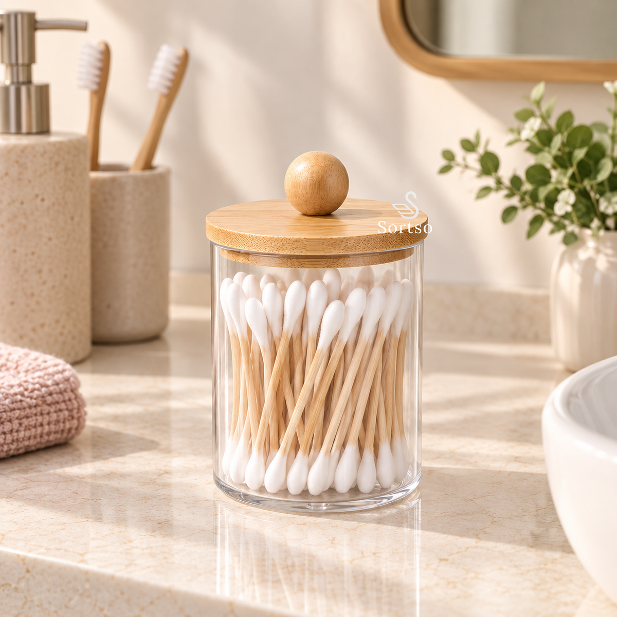 Clear vanity storage jar with bamboo lid filled with cotton buds on a bathroom counter.