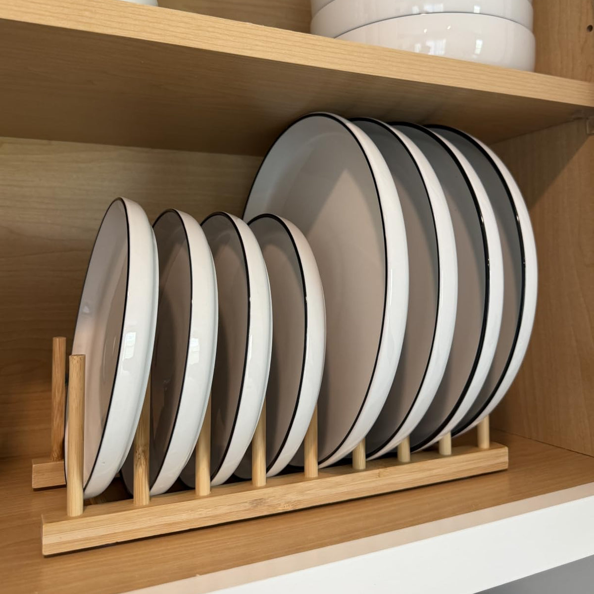 Wooden plate organizer rack holding dinner plates upright inside a kitchen cabinet.