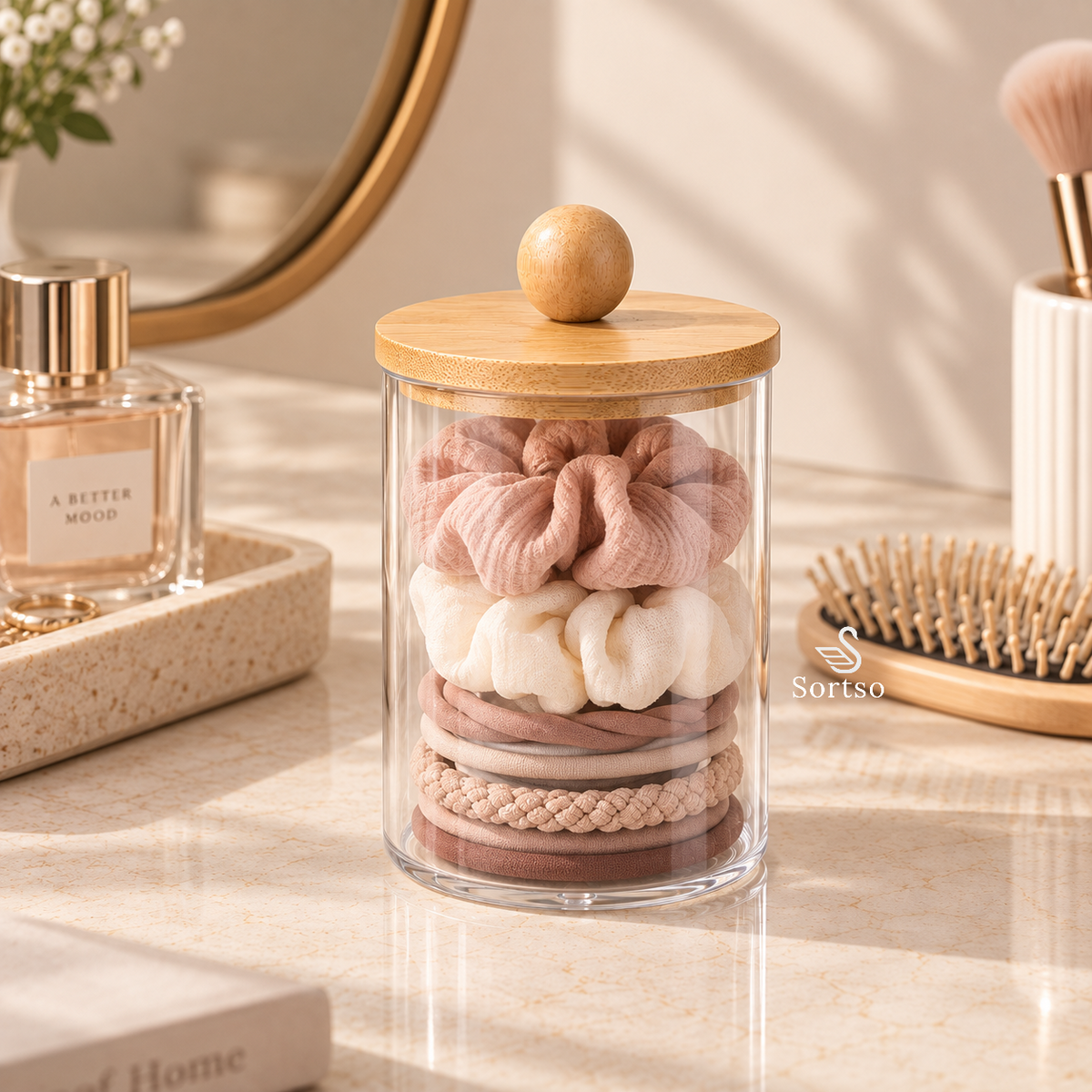 Clear vanity storage jar with bamboo lid holding scrunchies and hair ties.